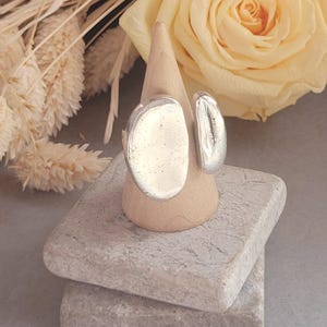 Peut inclure: Une bague en argent composée de deux éléments distincts aux formes organiques lisses et de tailles différentes. Le plus grand élément est ovale et plat, tandis que le plus petit est allongé et arrondi, avec une finition métallique polie.