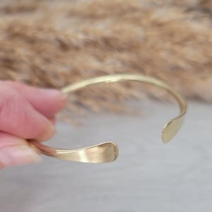 May include: A simple gold-toned metal bangle bracelet with rounded edges.