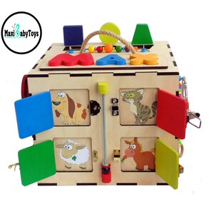 May include: Wooden activity cube with colorful sliding doors, a latch, a bead maze, and a spinning knob. The cube has images of animals, including a dog, cat, sheep, and horse. The cube is labeled "MAX".