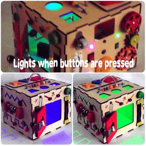 May include: A wooden activity cube with various interactive elements, including buttons that light up when pressed. The cube features a variety of colors, including red, green, blue, and yellow.  The cube is designed for children to explore and learn through play.