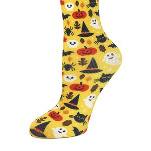 May include: A pair of yellow knee-high socks with a Halloween-themed print. The print features black bats, ghosts, witches' hats, pumpkins, and spiders.