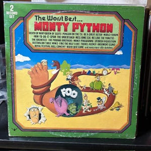 May include: Vintage Monty Python album cover, a 2-record set. The artwork features a whimsical illustration with a large foot, snake, and various cartoon characters. The album title is "The Worst Best... Monty Python" with a list of sketches.