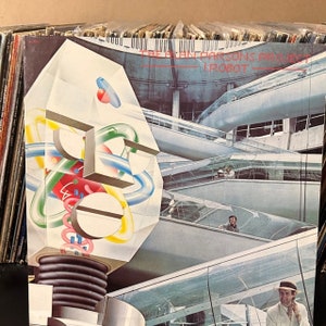 May include: Album cover for The Alan Parsons Project's "I Robot." The artwork features a stylized robot head with geometric shapes and colorful internal components. The background shows a futuristic architectural design with escalators.