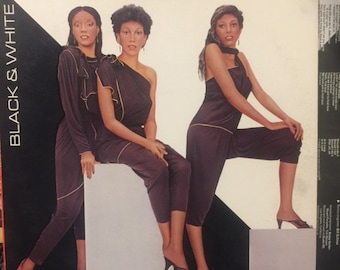 May include: A vintage album cover featuring the Pointer Sisters. The album title is "Black & White" and the album cover features three women wearing black jumpsuits with gold trim. The women are posing against a black and white background.