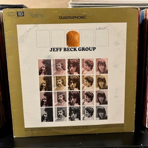 May include: A gold record album cover with the title "Jeff Beck Group" and the word "Quadraphonic" printed on the front. The cover features a grid of 16 photos of the band members, with an orange in the center.