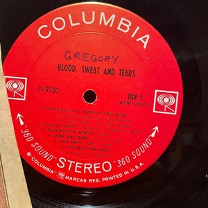 May include: A red vinyl record with the text "Columbia" in white, "Gregory" in black, and "Blood, Sweat and Tears" in white. The record is labeled "CS 9720" and "Side 1" with the song titles "Variations on a Theme by Erik Satie", "Smiling Phases", "Sometimes in Winter", "More and More", "And When I Die", and "God Bless the Child".