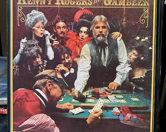 May include: A vintage vinyl record album cover featuring Kenny Rogers, the Gambler. The cover art depicts Rogers sitting at a poker table with other players, including women in period clothing. The album title, "Kenny Rogers the Gambler", is printed in large, bold letters at the top of the cover.