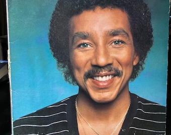 May include: A vinyl record album cover featuring a portrait of Smokey Robinson with dark curly hair and a mustache. The text SMOKEY ROBINSON appears in white at the top left, and being with you is printed in white at the top right on a blue background.