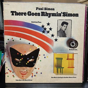 May include: Album cover for Paul Simon's "There Goes Rhymin' Simon." The cover features the album title, artist's name, and a portrait of Paul Simon. It includes a mask, stars, and the text "American Tune" and "Take Me to the Mardi Gras."
