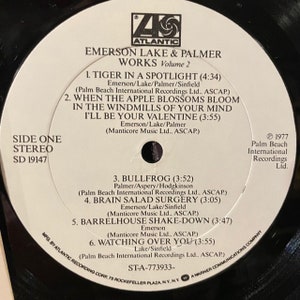 May include: A white vinyl record with black text. The record is for Emerson Lake & Palmer's album "Works, Volume 2". The album cover features the band's name and the album title in black text. The record is labeled "Side One, Stereo, SD 19147".