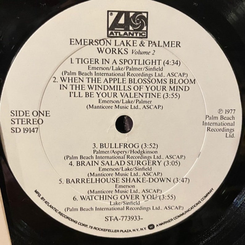 May include: A white vinyl record with black text. The record is for Emerson Lake & Palmer's album "Works, Volume 2". The album cover features the band's name and the album title in black text. The record is labeled "Side One, Stereo, SD 19147".