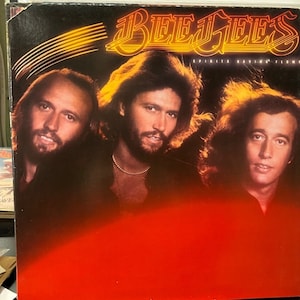 May include: A vintage vinyl record album cover featuring a photo of the Bee Gees band members. The album title is "Spirits Having Flown" and the background is a red gradient.