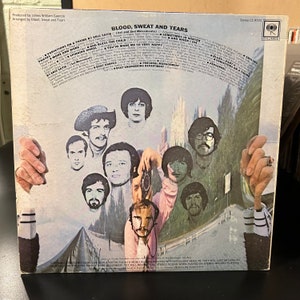 May include: A vintage vinyl record album cover for Blood, Sweat and Tears. The cover features a collage of band members in a psychedelic style. The album title is printed in bold, white letters on a red background. The album is a classic rock record.
