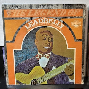 May include: Vintage vinyl record album cover for "The Legend of Leadbelly." The cover features a portrait of a man playing a yellow guitar, with text including "Leadbelly," "Josh White," and "Sonny Terry." The album art has orange and brown tones.