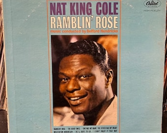 May include: A vintage vinyl record album cover featuring Nat King Cole. The cover is blue and white with a photo of Nat King Cole smiling. The album title is "Ramblin' Rose" and the text "music conducted by Belford Hendricks" is below the title. The album is a Capitol Records release.