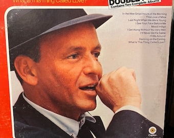 May include: A red vinyl record album cover featuring Frank Sinatra in a black fedora, looking to the right. The album title is "What Is This Thing Called Love?" and the album is a "Double Play" with two complete albums. The album cover also includes a list of songs on the album.