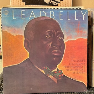 May include: Vintage vinyl record album cover featuring a portrait of Leadbelly. The cover has a blue and orange background with the name "LEADBELLY" in large white letters. The album includes legendary performances never before released.