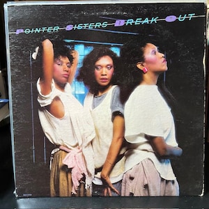 May include: A vinyl record cover for the Pointer Sisters album Break Out. The cover features three individuals with dark hair wearing white tops and light-colored skirts against a dark background. The text POINTER SISTERS BREAK OUT is at the top.
