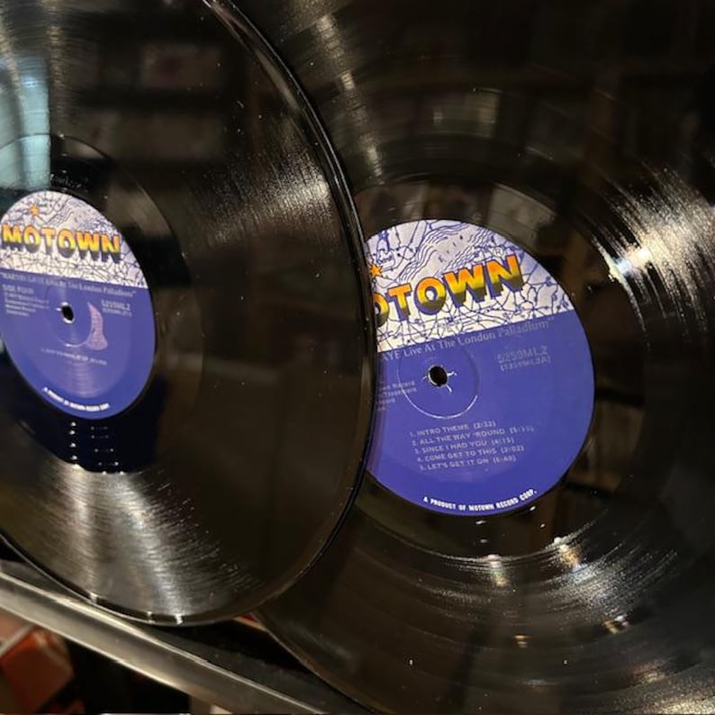 May include: Two black vinyl records with blue and white labels. The labels read "MOTOWN" and list song titles. The records are in good condition, with visible grooves and a glossy finish. The records are likely vintage.