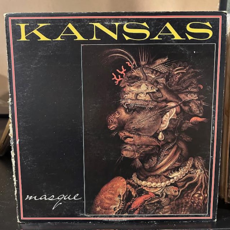 May include: A vintage vinyl record album cover featuring the band Kansas. The cover art is a dark, surreal painting of a face made up of fish, shells, and other sea creatures. The album title "Masque" is written in white script at the bottom of the cover.