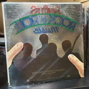Pu&ograve; includere: Una copertina di un disco in vinile intitolata The Beatles Rock 'n' Roll Music. La copertina presenta una scena scura e illustrata di quattro figure viste da dietro, con il nome della band e il titolo dell'album in grandi lettere rosse e blu.
