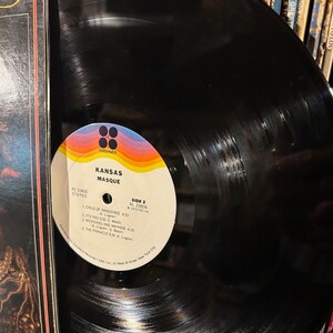 May include: A black vinyl record with a colourful label. The label has the text "KANSAS MASQUE" and the record number "P2 33806 STEREO". The label also has the text "SIDE 2 BL 33806 1975 CRS INC."