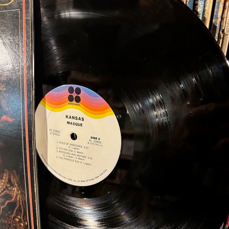 May include: A black vinyl record with a colourful label. The label has the text "KANSAS MASQUE" and the record number "P2 33806 STEREO". The label also has the text "SIDE 2 BL 33806 1975 CRS INC."