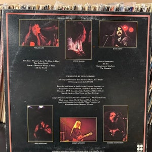 May include: The back cover of a vinyl record album for the band Kansas. The album cover features a black background with white text and photos of the band members. The album title is "Kansas" and the album's release date is 1976. The album's tracklist is listed on the back cover.