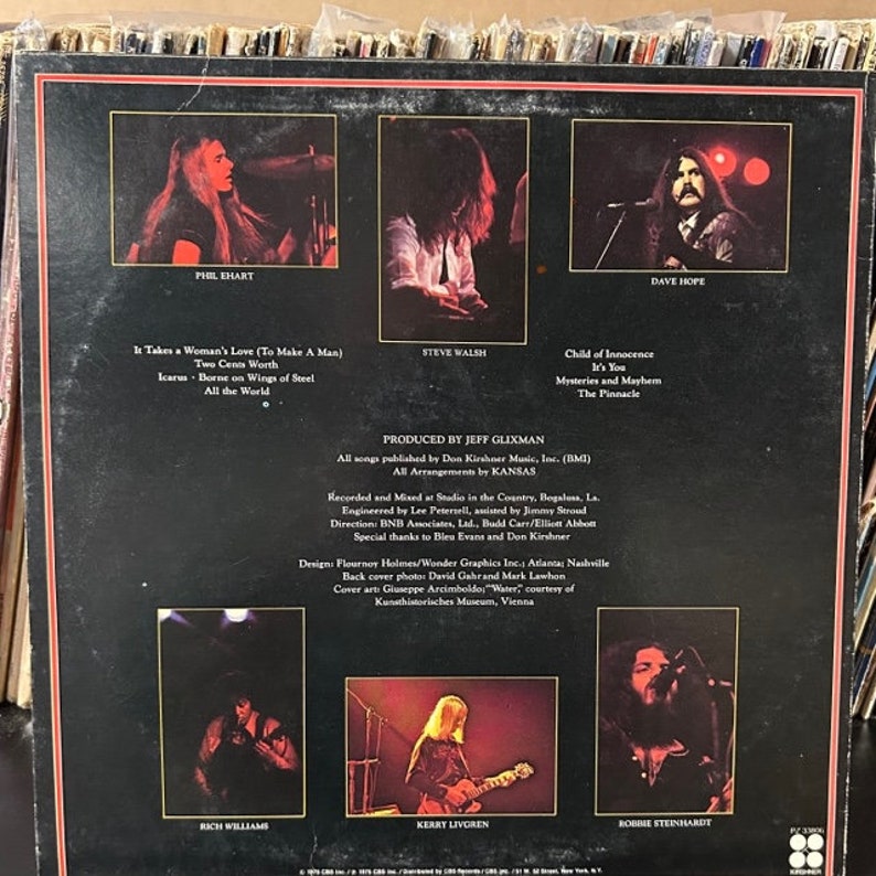 May include: The back cover of a vinyl record album for the band Kansas. The album cover features a black background with white text and photos of the band members. The album title is "Kansas" and the album's release date is 1976. The album's tracklist is listed on the back cover.