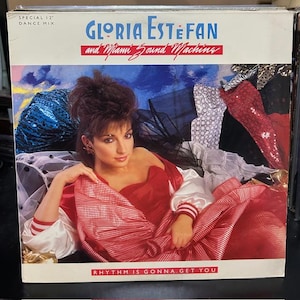 May include: Album cover for Gloria Estefan and Miami Sound Machine's "Rhythm Is Gonna Get You." The cover features a woman in a red dress with white sleeves. The album title and artist name are in blue and red text. The words "Special 12" Dance Mix" are at the top.