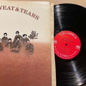 May include: A vinyl record album cover and record featuring a band called "Blood, Sweat & Tears". The cover features a group of men in a field with trees in the background. The record label is red and white with the Columbia Records logo and the band name.