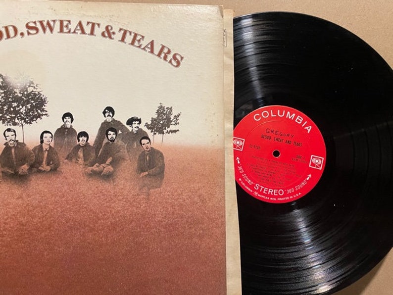 May include: A vinyl record album cover and record featuring a band called "Blood, Sweat & Tears". The cover features a group of men in a field with trees in the background. The record label is red and white with the Columbia Records logo and the band name.