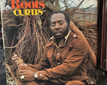 Puede incluir: Portada del álbum "Roots" de Curtis. La carátula presenta a un hombre con chaqueta marrón y gafas, sentado frente a un fondo de raíces de árboles. El título del álbum está en letras naranjas y amarillas.