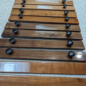 May include: Nine wooden cabinet doors with black knobs. The doors are arranged in a stack, with the top door being the lightest in color and the bottom door being the darkest.