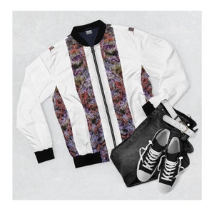 May include: A white bomber jacket with a zip fastening and black trim. The jacket features a colourful, abstract print. The jacket is paired with black jeans and white trainers.
