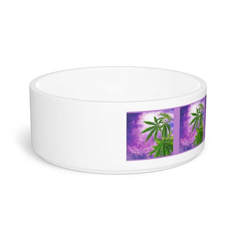 May include: White ceramic pet bowl featuring a design of green cannabis leaves against a purple and white cloudy sky.