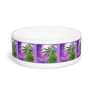 May include: White ceramic pet bowl with a purple and green design. The design features a repeating pattern of marijuana leaves against a purple cloudy sky.