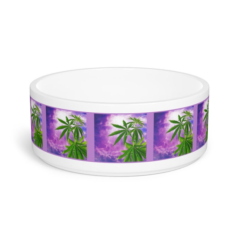 May include: White ceramic pet bowl with a purple and green design. The design features a repeating pattern of marijuana leaves against a purple cloudy sky.