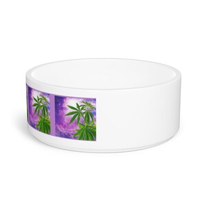 May include: White ceramic pet bowl featuring a design of green cannabis leaves against a purple and white cloudy sky.