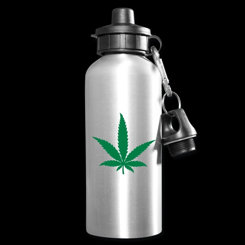 Puede incluir: Una botella de agua plateada con un dise&ntilde;o de hoja de marihuana verde. La botella tiene una tapa negra y un mosquet&oacute;n negro.
