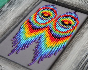 Può includere: Un paio di lunghi orecchini colorati con perline che formano un motivo arcobaleno. Gli orecchini sono realizzati con piccole perline rotonde in tonalità di rosso, arancione, giallo, verde, blu, indaco e viola. Le perline sono disposte in un motivo circolare, creando un effetto arcobaleno. Gli orecchini sono appesi a ganci argentati.