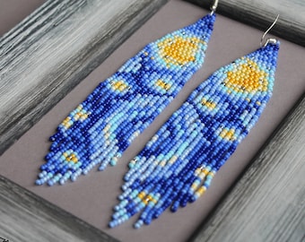 May include: A pair of long, beaded earrings with a blue, yellow, and white pattern. The earrings are hanging from silver hooks.