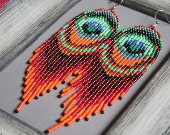 Può includere: Un paio di lunghi orecchini a perline con un design a forma di piuma di pavone. Gli orecchini sono realizzati con perline rosse, arancioni, verdi, blu e nere. Gli orecchini sono appesi a ganci d'argento.