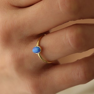 May include: A gold ring with a blue opal gemstone. The ring is on a person's finger.