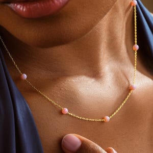 May include: A delicate gold necklace featuring small, pink gemstones evenly spaced along the chain. The necklace is displayed against a dark blue background, with the text "GOLD PERSONALIZED" visible in the lower left corner.