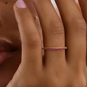 May include: A gold-colored ring with a band of small, bright pink gemstones. The ring is on a person's finger, with the hand resting against the face. The words "GOLD PERSONALIZED" are in the lower left corner.