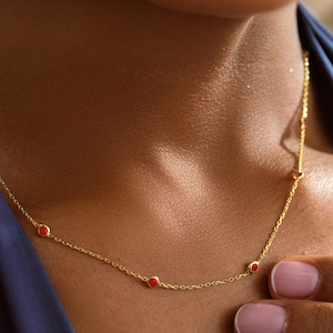 May include: A delicate gold necklace featuring small, round red gemstones evenly spaced along the chain. The necklace is displayed against a blue background. The words "GOLD PERSONALIZED" are in the bottom left corner.
