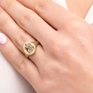 May include: A gold signet ring with an oval-shaped top featuring a detailed engraved design.