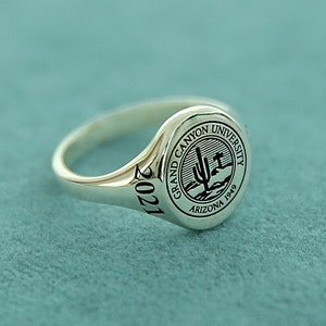 May include: A silver class ring with a raised circular seal featuring the Grand Canyon University logo and the text "Grand Canyon University Arizona 1949". The year "2021" is engraved on the band.