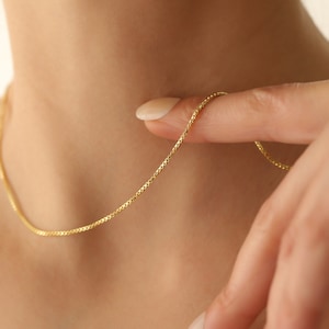 May include: A delicate gold chain necklace with a box chain design. The chain is thin and has a subtle shine.